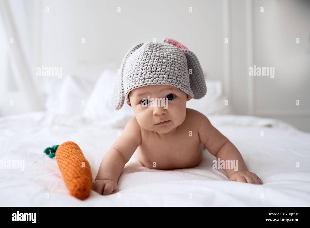 Baby four months old in a bunny costume with a knitted carrot laying on