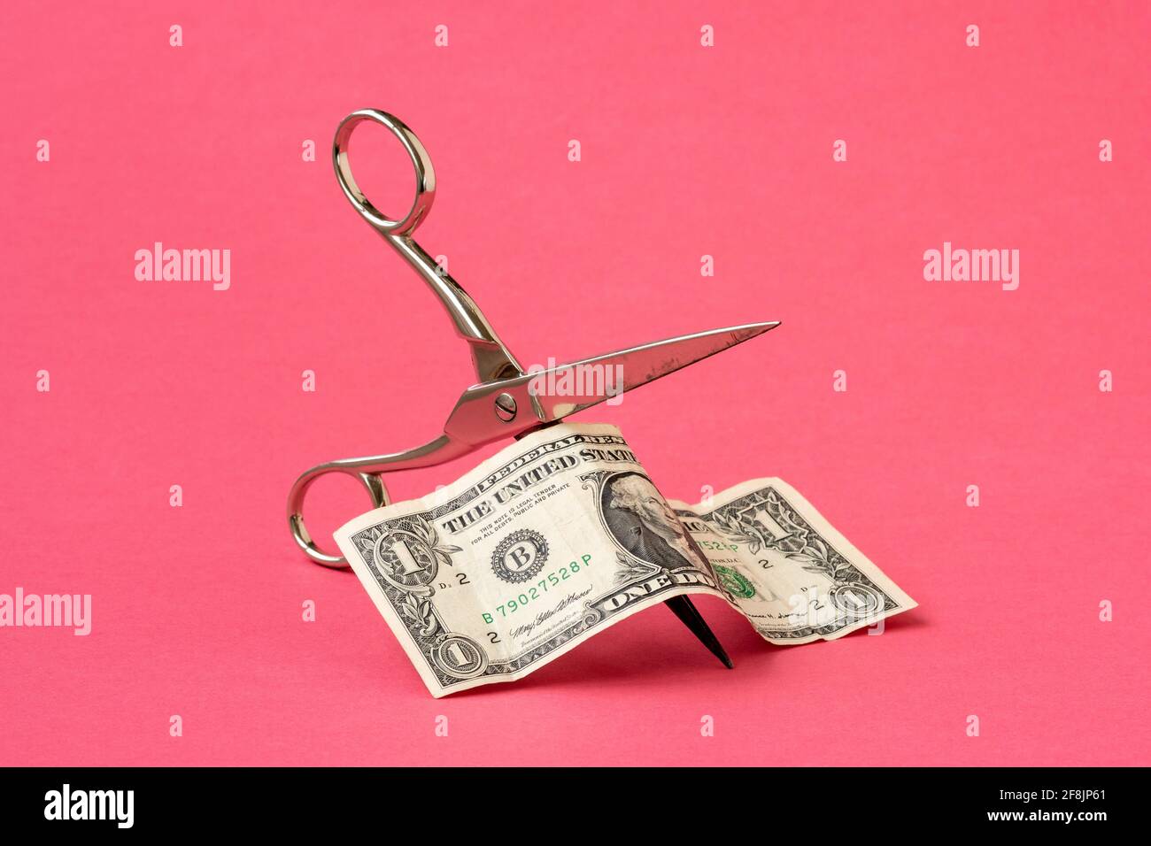 Cutting one dollar with scissors on pink background. Concept on the topic of devaluation of money. Stock Photo