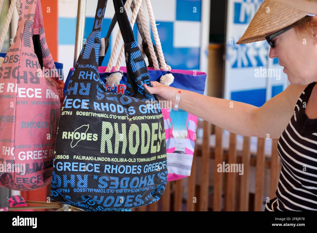 A female tourist admires a casual souvenir shoulder tote bag, marked up with Rhodes across it which is for sale outside a shop in Rhodes city, Greece Stock Photo