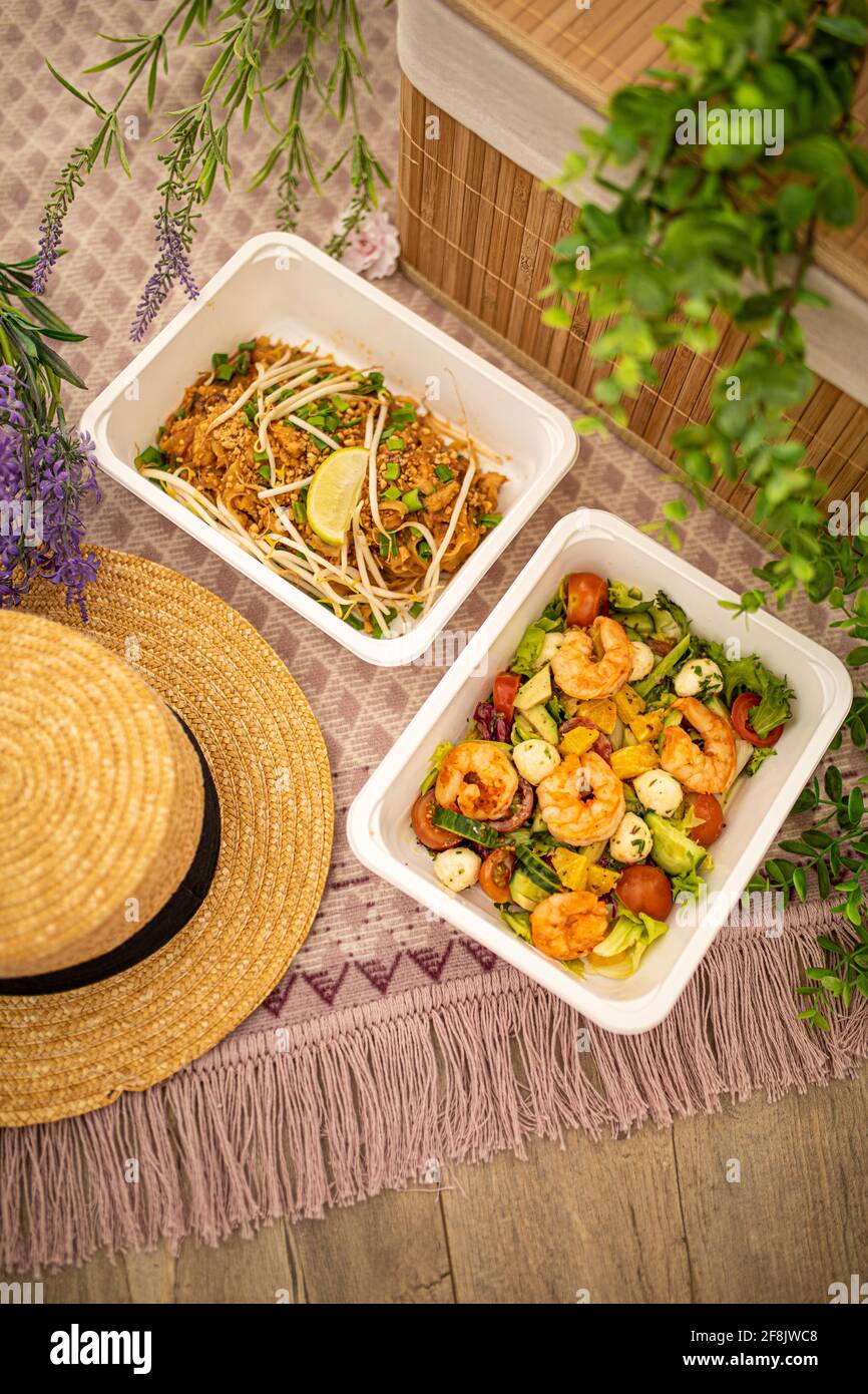 shrimp salad and Asian pad thai. composition with natural decor. concept food delivery. picnic outdoors summer spring time and plastic dishes. Stock Photo