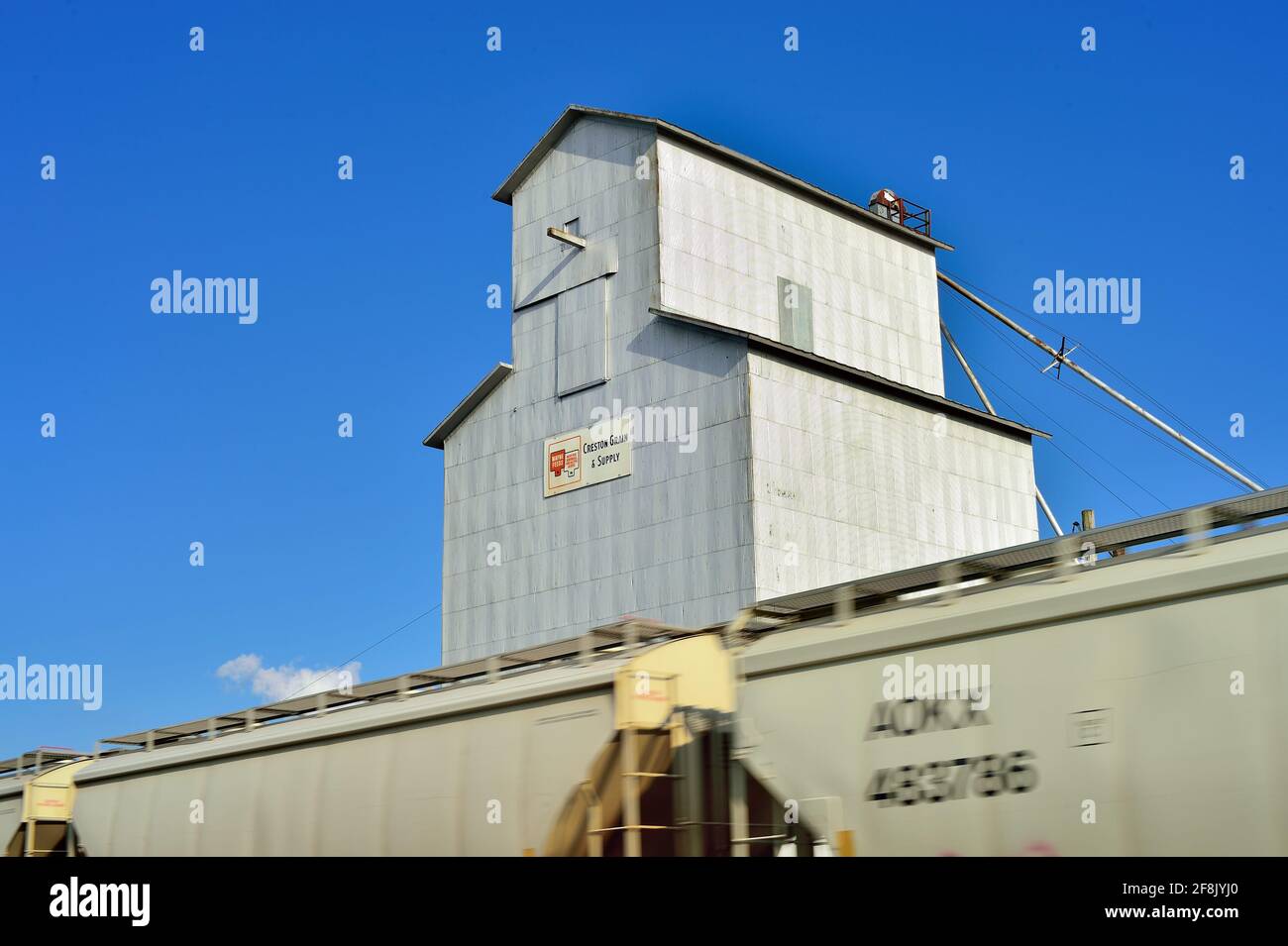 Creston, Illinois, USA. Cars in a freight train of the type used to haul grain race past a small town grain elevator in northeastern Illinois. Stock Photo