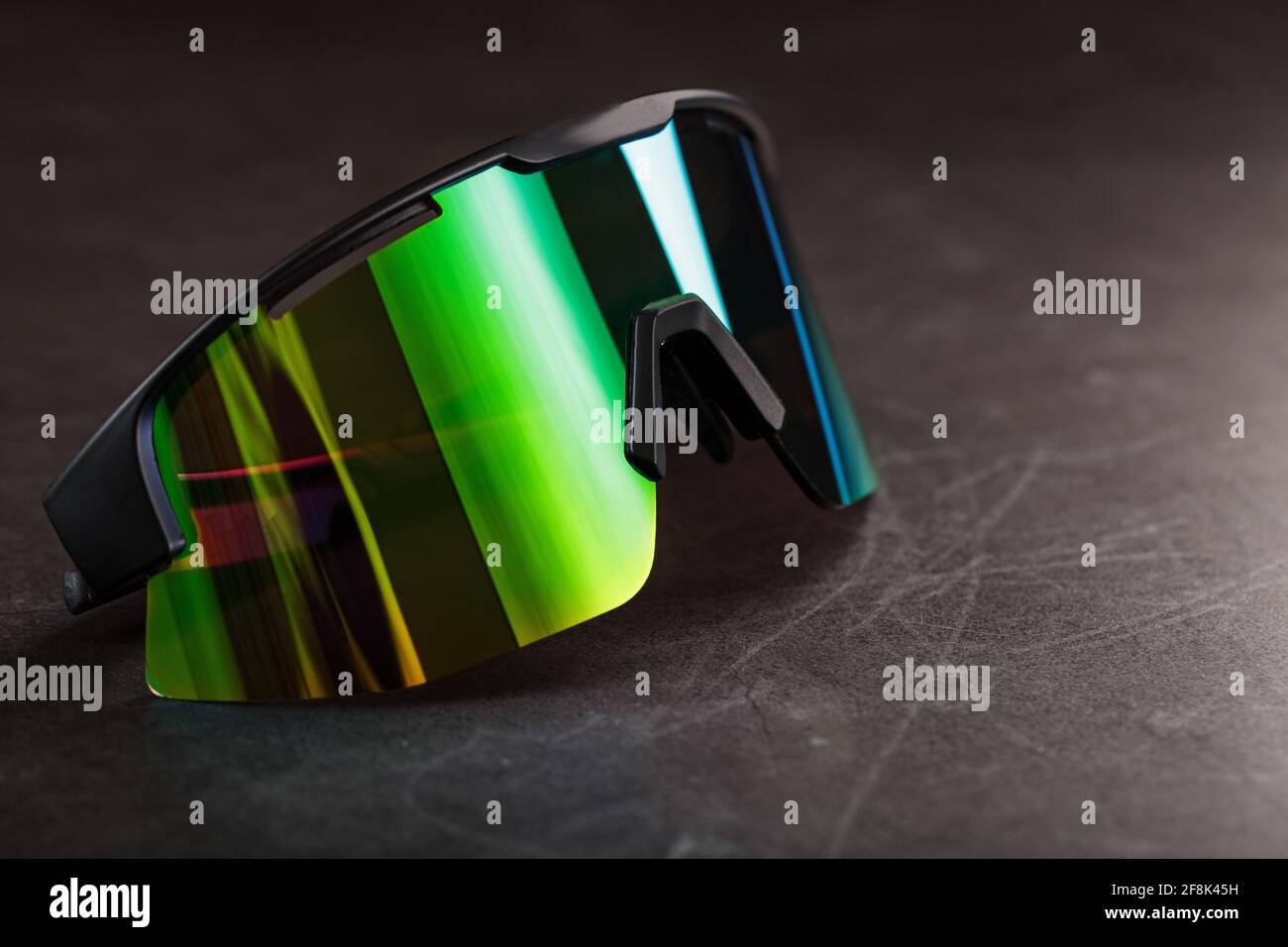 Sports glasses with a green mirrored lens on a black textured