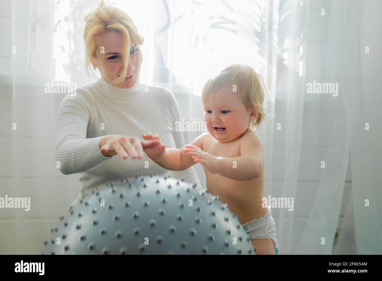 Mom is engaged in gymnastics with the baby on an inflatable ball. Fitball, gymnastics for a child. Stock Photo