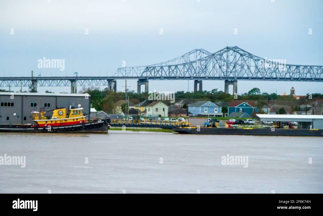 Working waterfront on the Mississippi River in New Orleans, with bridge, tug boat and barge.  Colorful older homes on the shore. Stock Photo