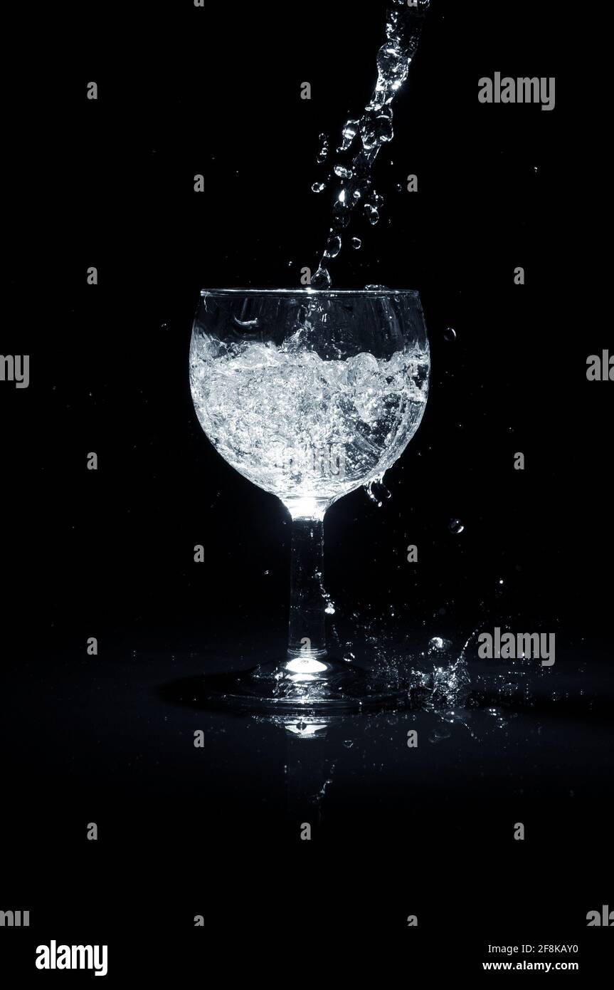 Pouring water into a glass on black background. Stock Photo