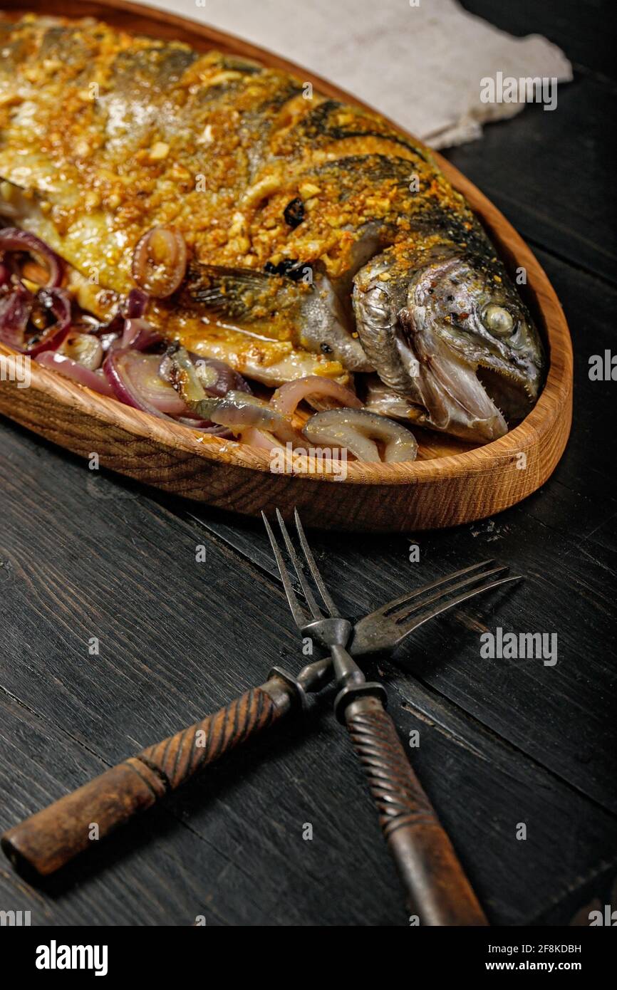 Close-up wooden dish with grilled fish. Sea food with vegetables on a dark wooden table. Sea trout. Delicious and healthy lunch or dinner. Mediterrane Stock Photo