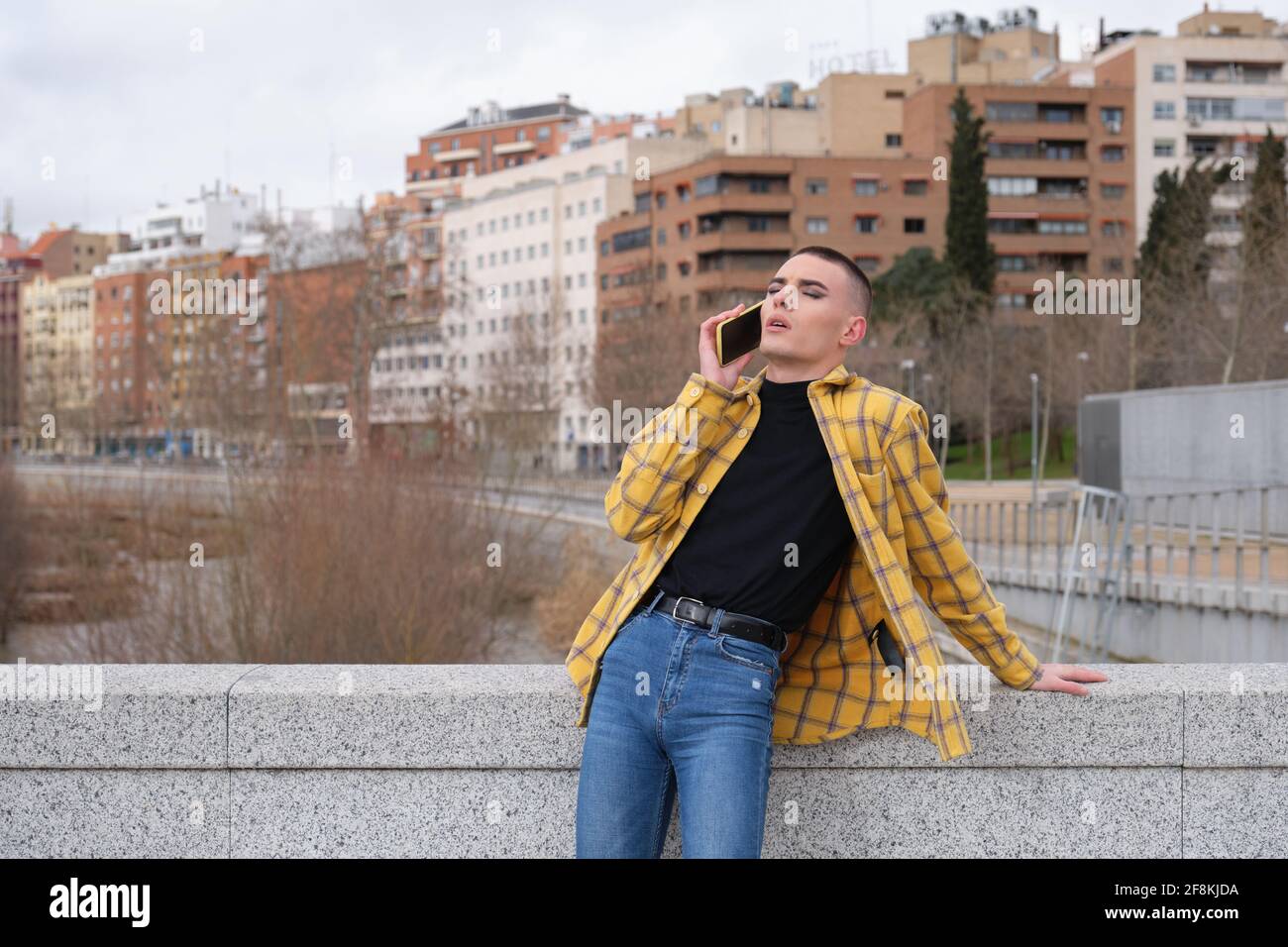 Young non binary person speaking on a smartphone with the eyes closed. Make up androgynous person. Stock Photo