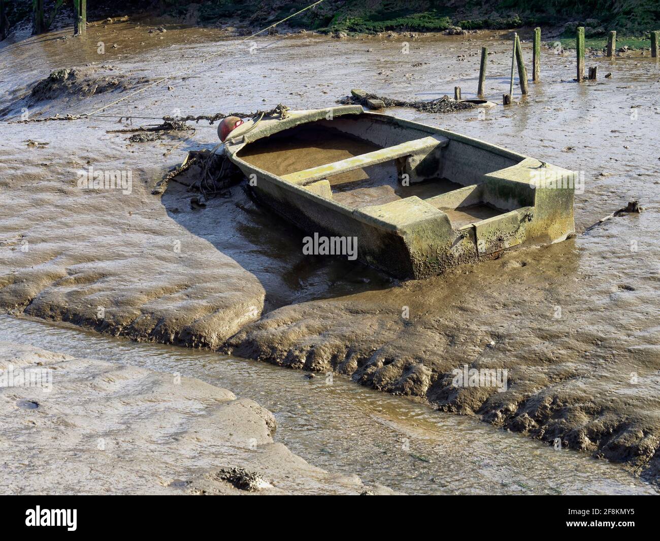 Low tide at Morston on the North Noroflk coast leaves boats stranded on the sticky mud of the salt marsh. This sunken boat is full of mud. Stock Photo