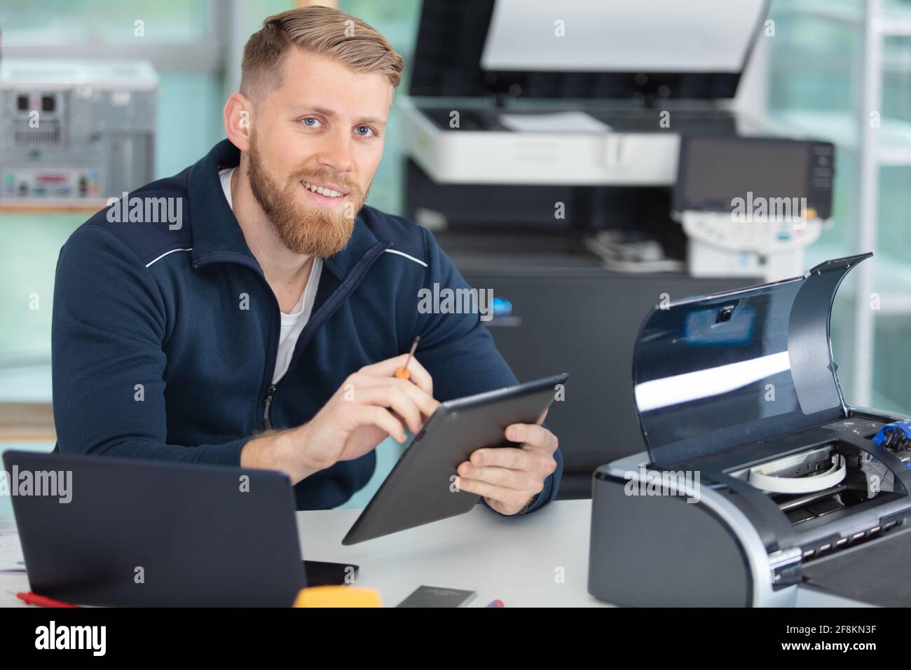 young technician using a tablet to fix a printer Stock Photo