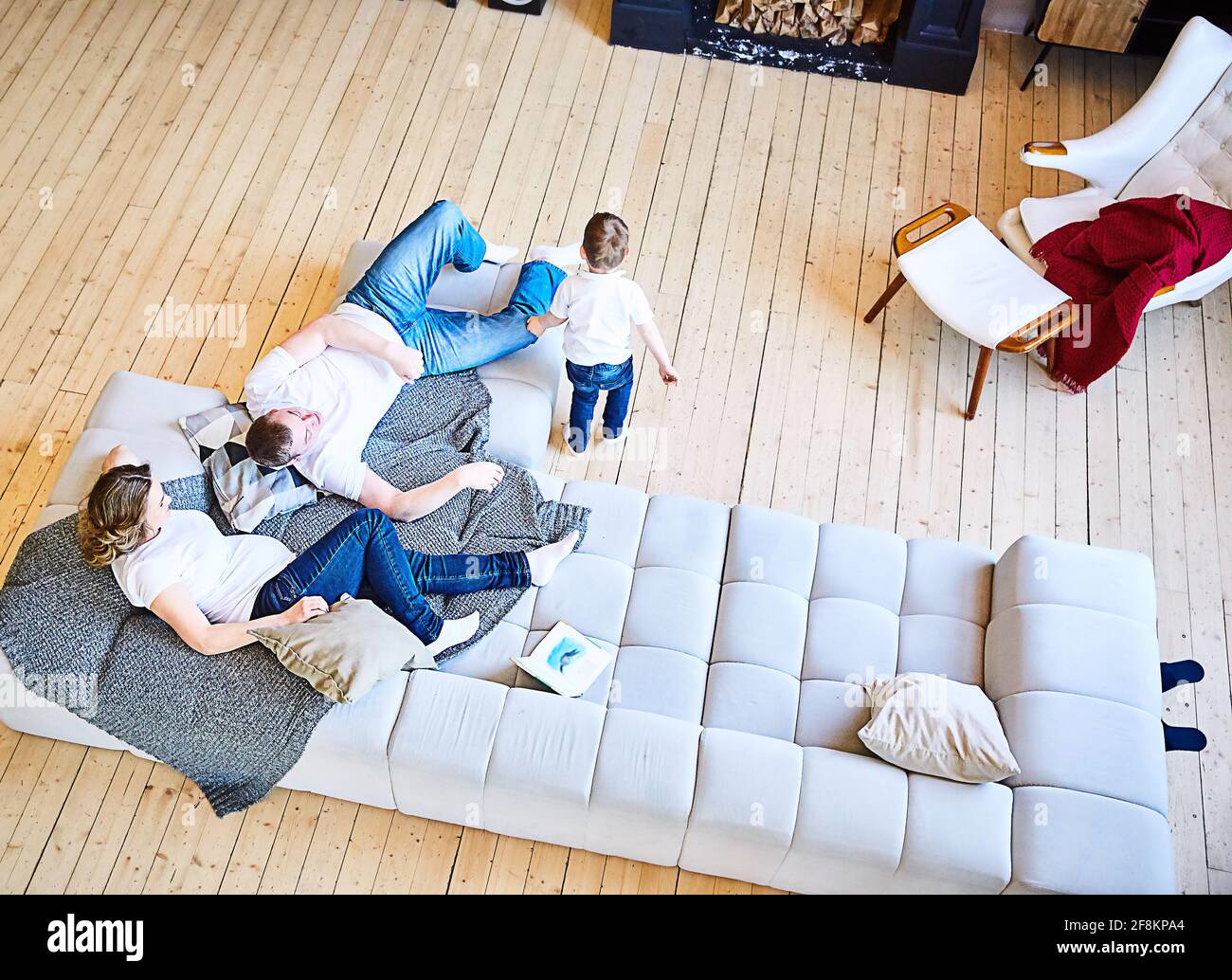 A family with a small child is relaxing on a huge gray sofa in the living room. Lifestyle. Family look in jeans and white T-shirts. view from above Stock Photo
