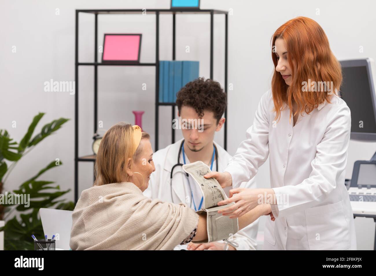 A nurse places a blood pressure monitor on a patient's arm to check blood pressure. The primary care physician and the intern Stock Photo