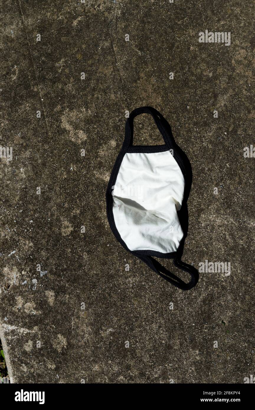 Vertical shot of cotton mask thrown away on concrete road. Stock Photo