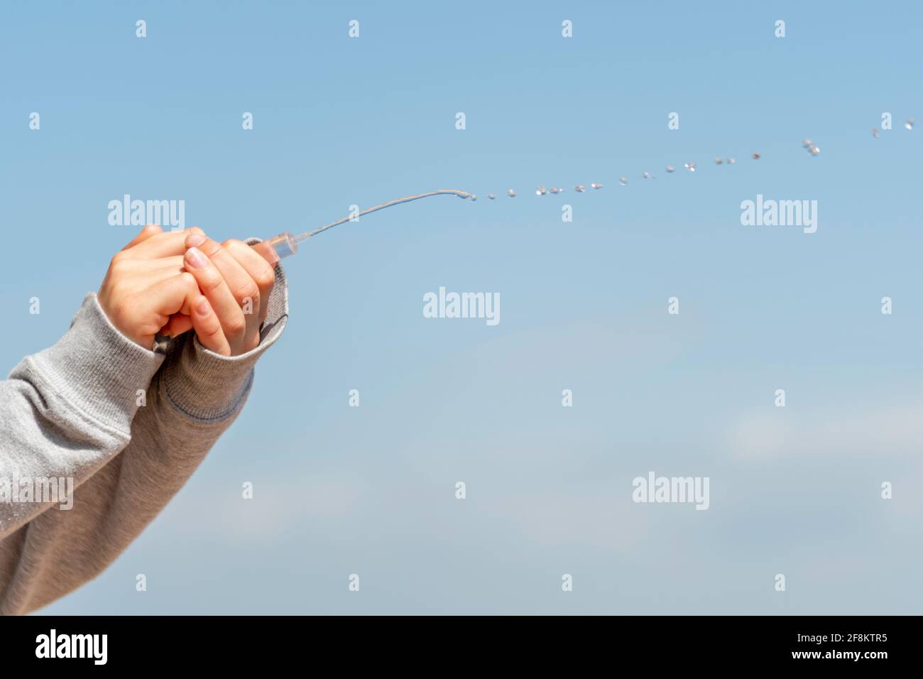female hands squirting water from a syringe with a blue sky in the background Stock Photo