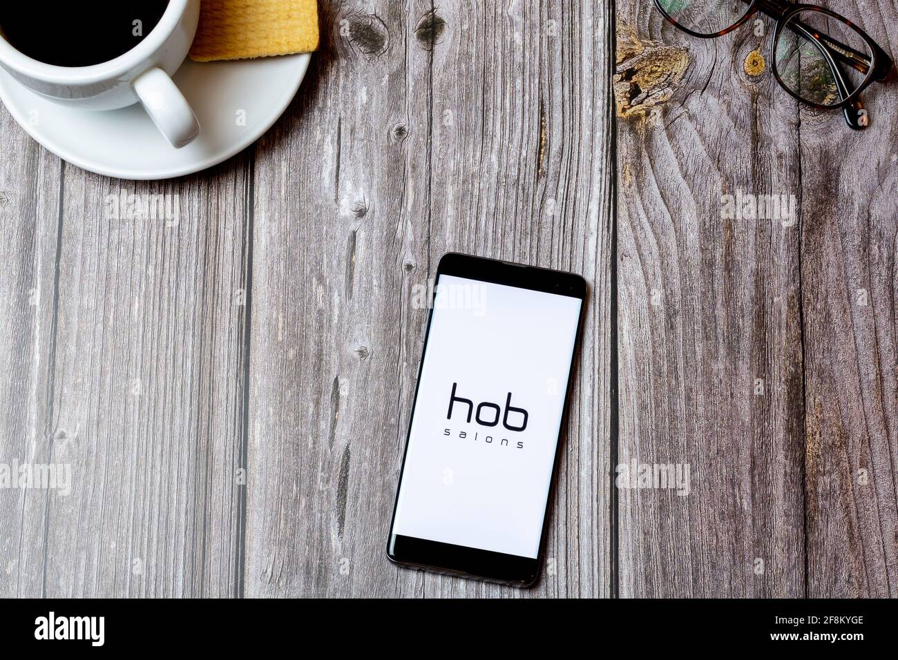 A Mobile phone or cell phone laid on a wooden table showing the hob salons app on screen Stock Photo