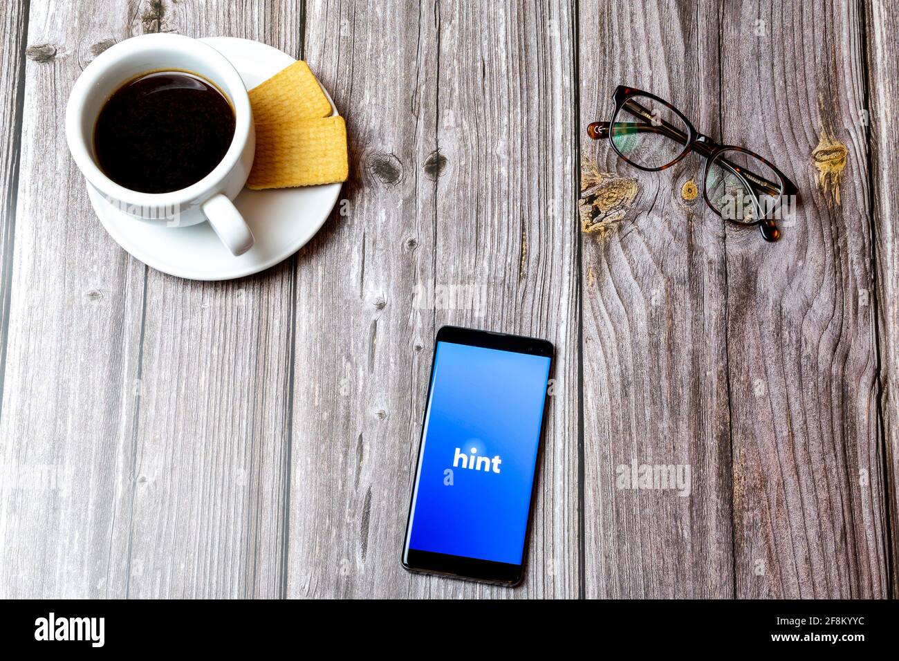 A Mobile phone or cell phone laid on a wooden table showing the Hint app on screen Stock Photo
