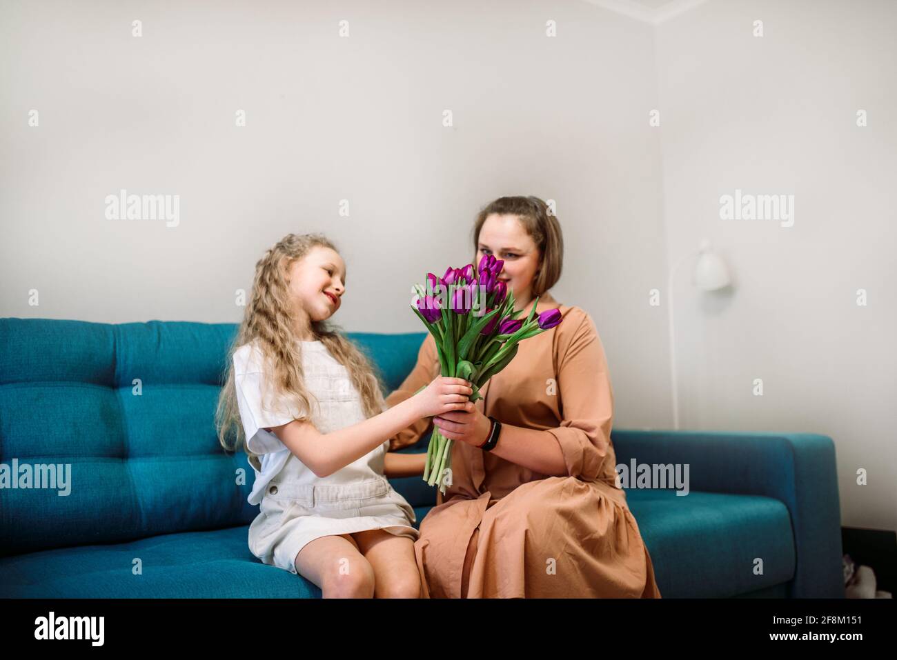 Cute little girl greeting her mother at home. Bouquet of purple tulips