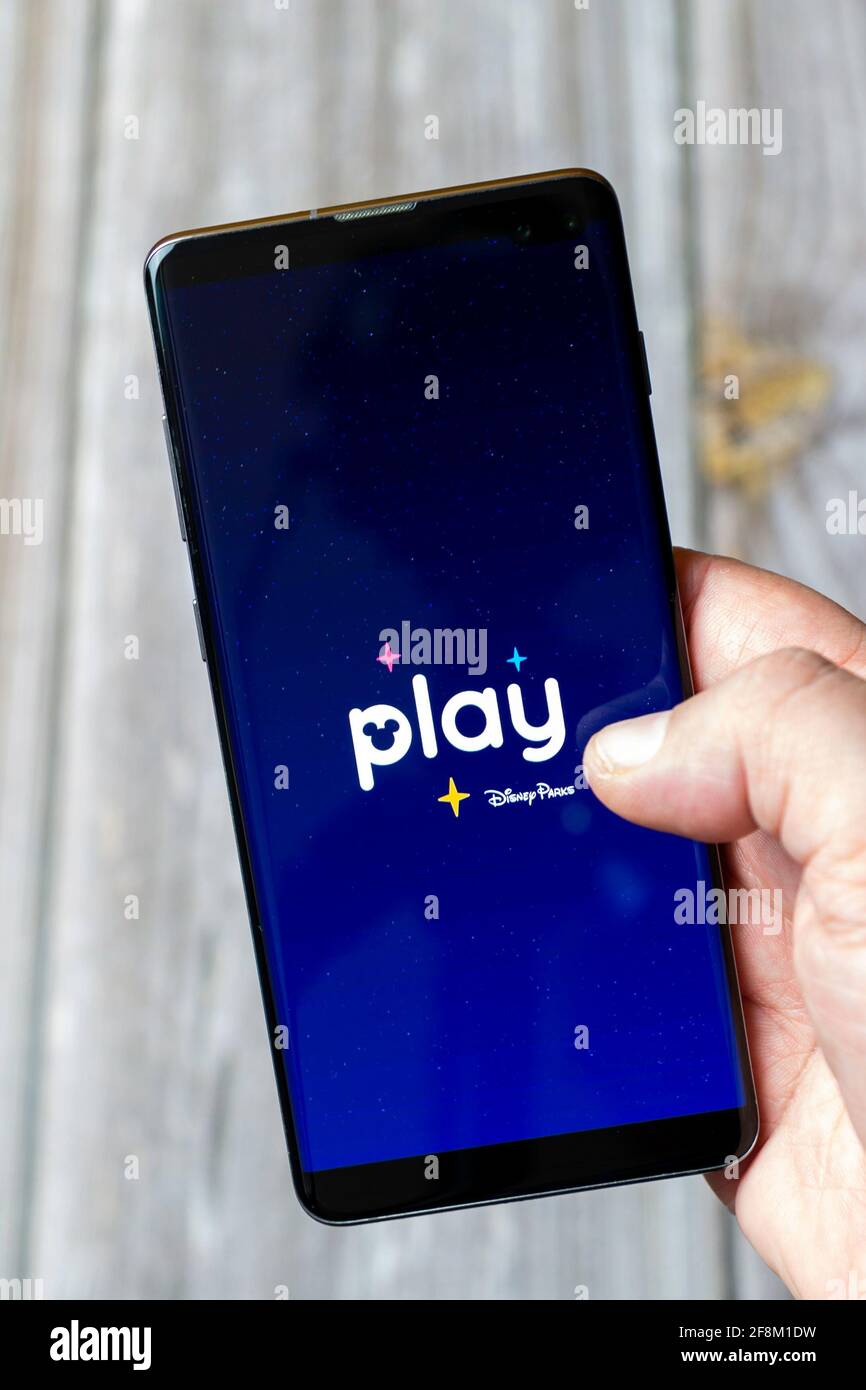 A Mobile phone or Cell phone being held in a hand showing the Play disney parks app on screen Stock Photo