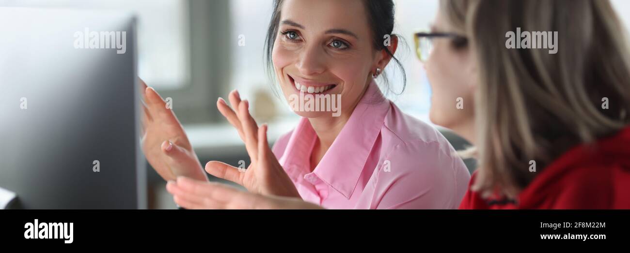 Two smiling women are sitting at computer. Stock Photo