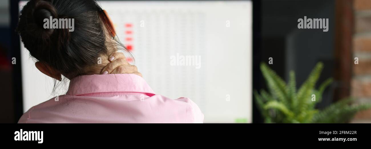 Tired woman sits at computer and massages pain in her neck Stock Photo