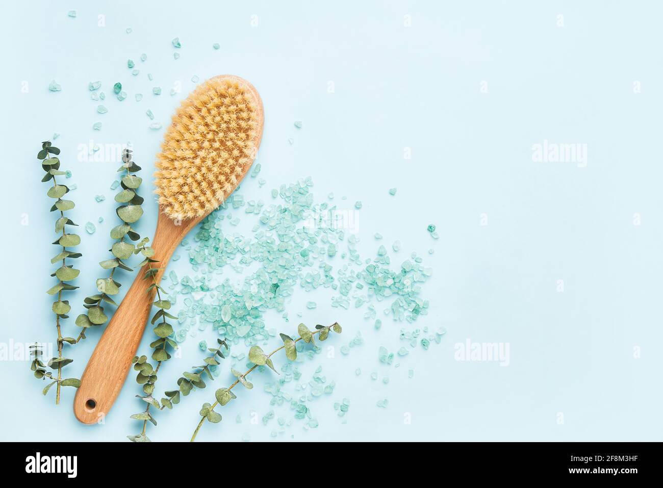 SPA treatment concept. Anti-cellulite body brush, eucalyptus branches, and bath salt on a blue background. Top view, copy space for text Stock Photo