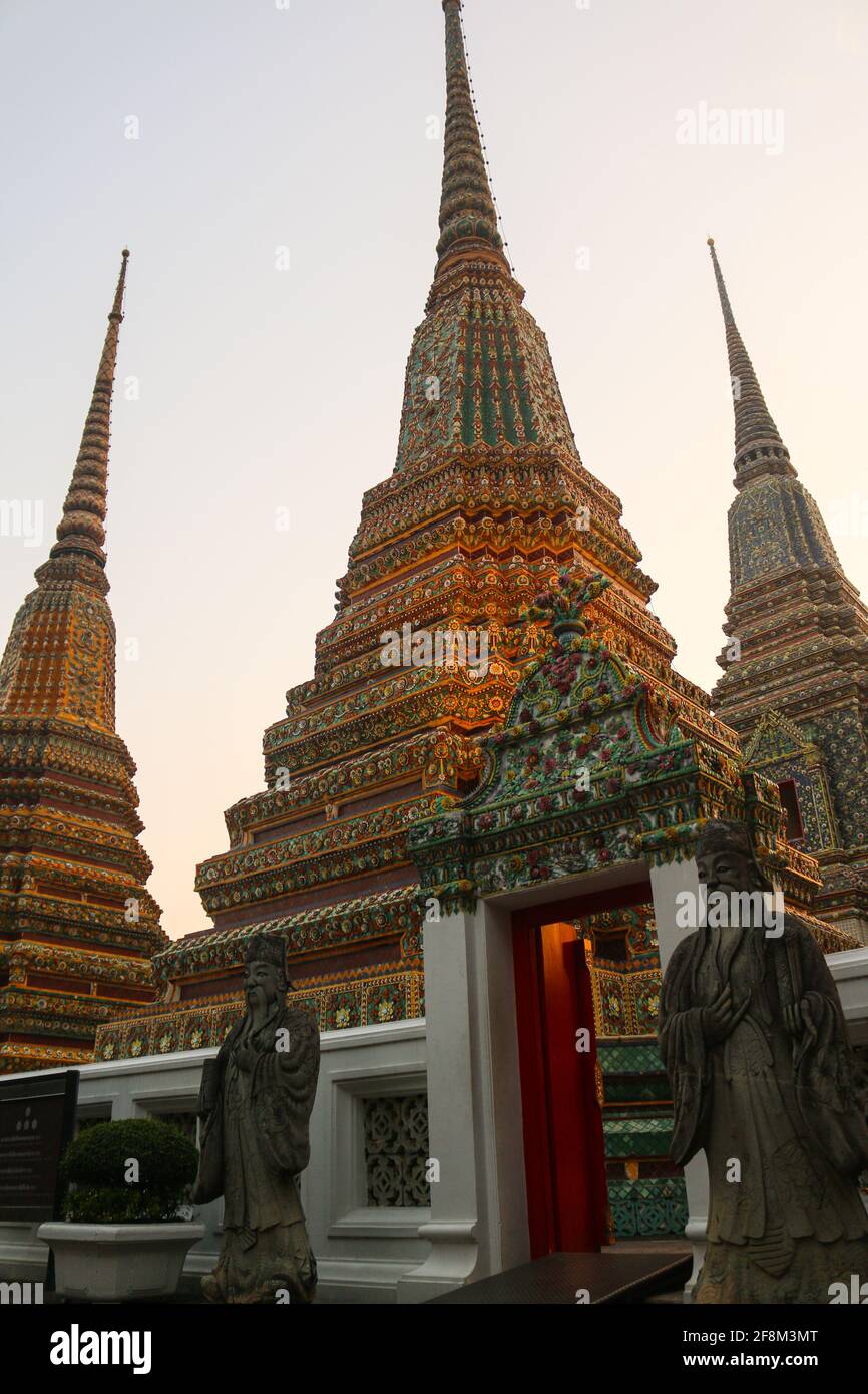 The entrance to Phra Chedi Rai with two guardians and three stupa against clear sky. Hexagonal pagodas with mosaic in Wat Pho Buddha temple complex. Stock Photo
