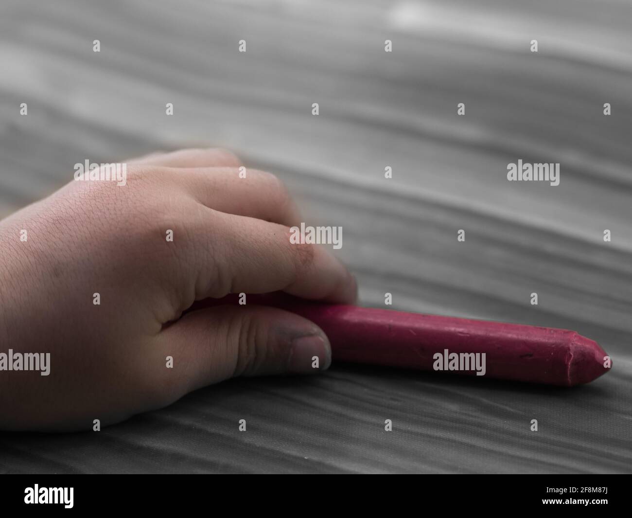 close-up of a child's hand holding a crayon, on a light wooden background Stock Photo