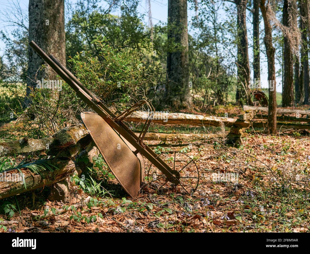 Old vintage antique wheelbarrow with a broken spoke wheel resting on a split rail fence in rural Alabama, USA. Stock Photo