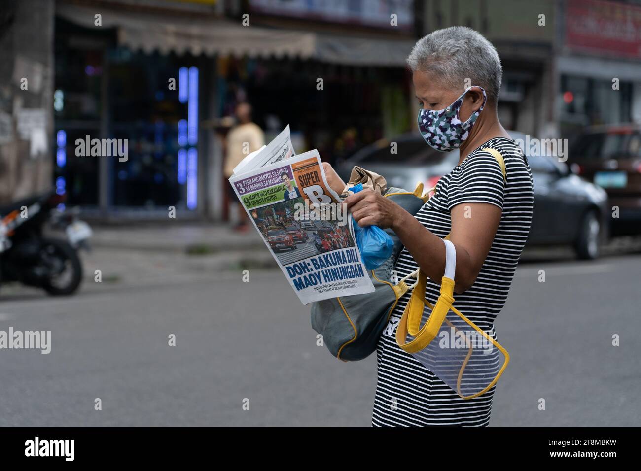 A Filipino woman reading a newspaper whilst wearing a face mask and holding a face shield, Cebu City, Philippines Stock Photo