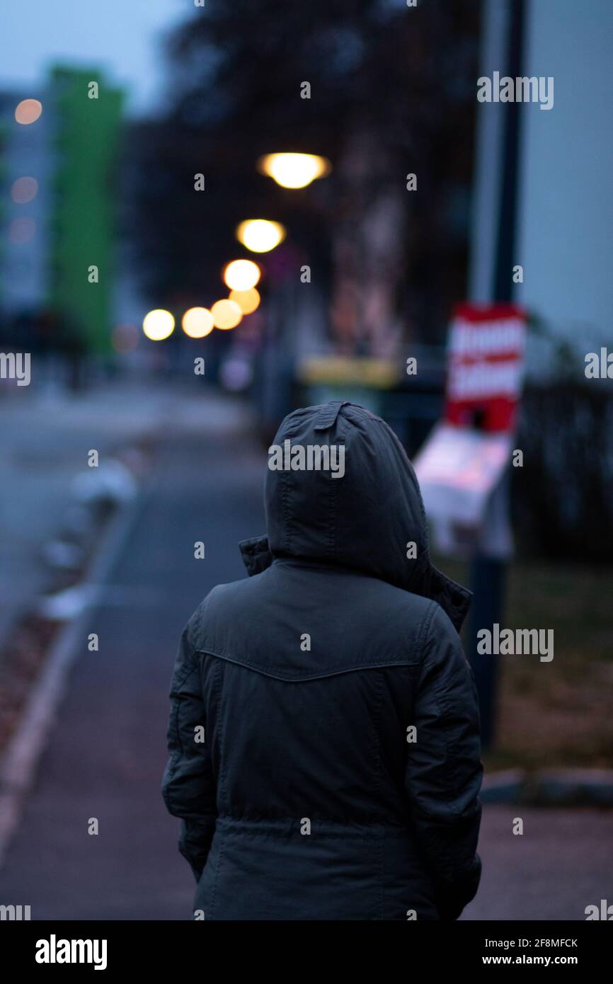 Rear view of a woman wearing a black hooded jacket in the street with a bokeh background Stock Photo