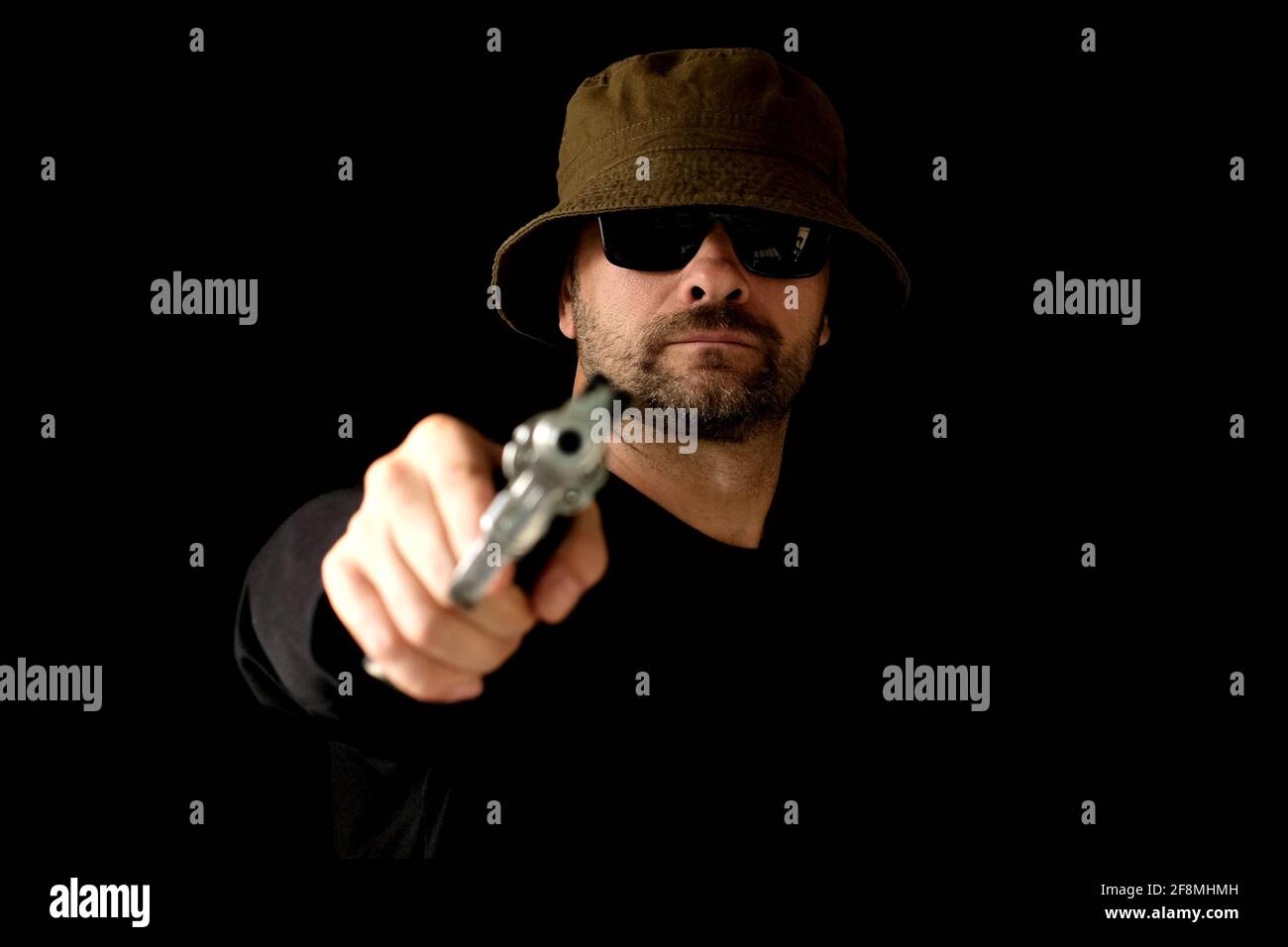 Gangster Male contract killer with revolver looks at the camera. Bald man killer aiming a revolver pistol at you. Stock Photo