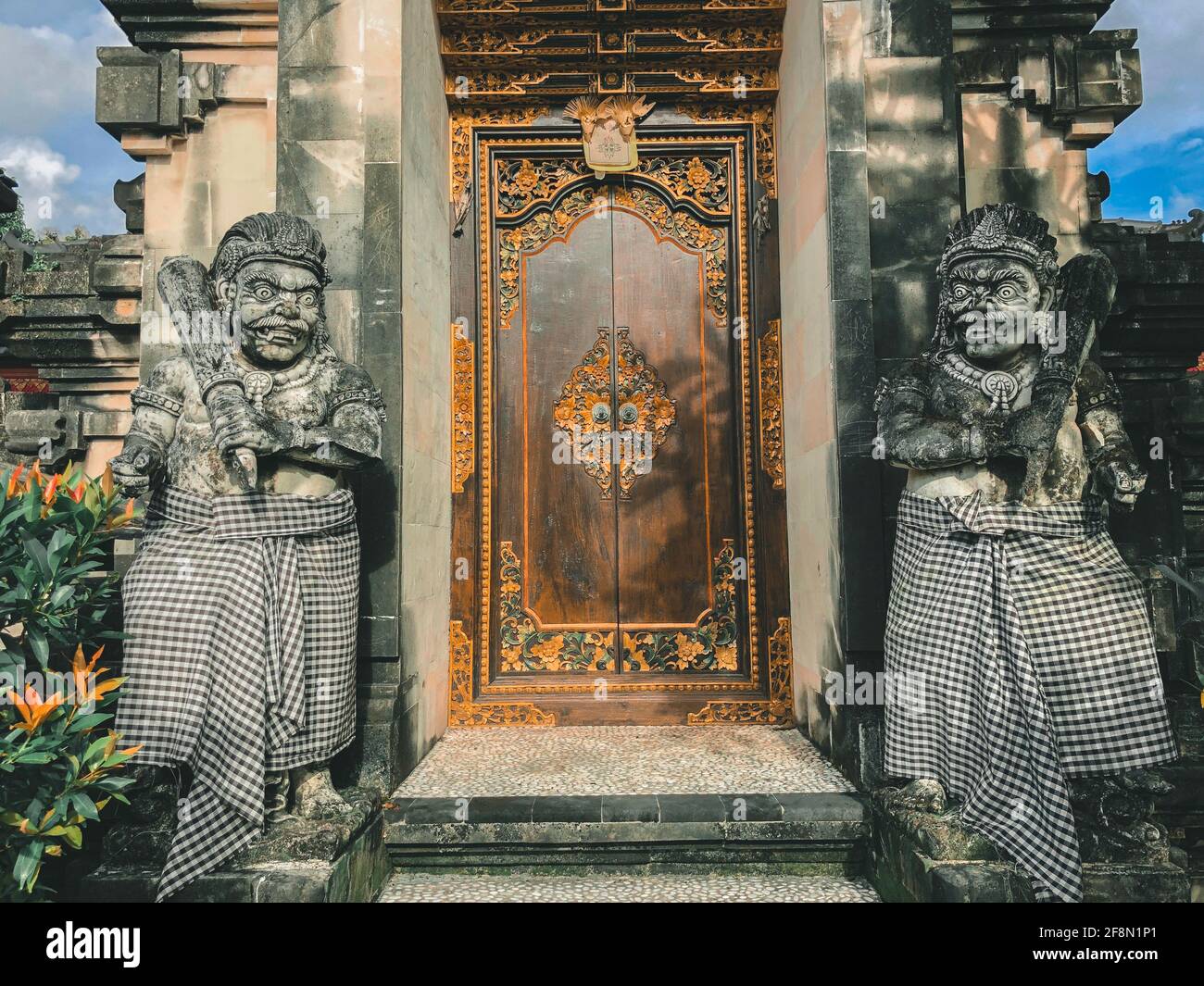 Door or gate to enter into traditional balinese garden architecture detail. Wooden Indonesian gate guarded by stone statues. Old wooden door, entrance Stock Photo