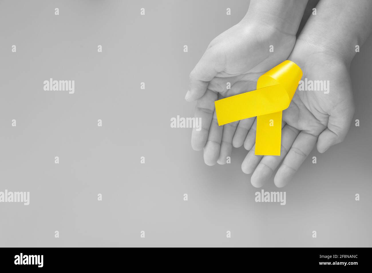 Hand holding Yellow ribbon on black and white background, copy space. Bone cancer Sarcoma Awareness childhood cancer cholangiocarcinoma gallbladder ca Stock Photo