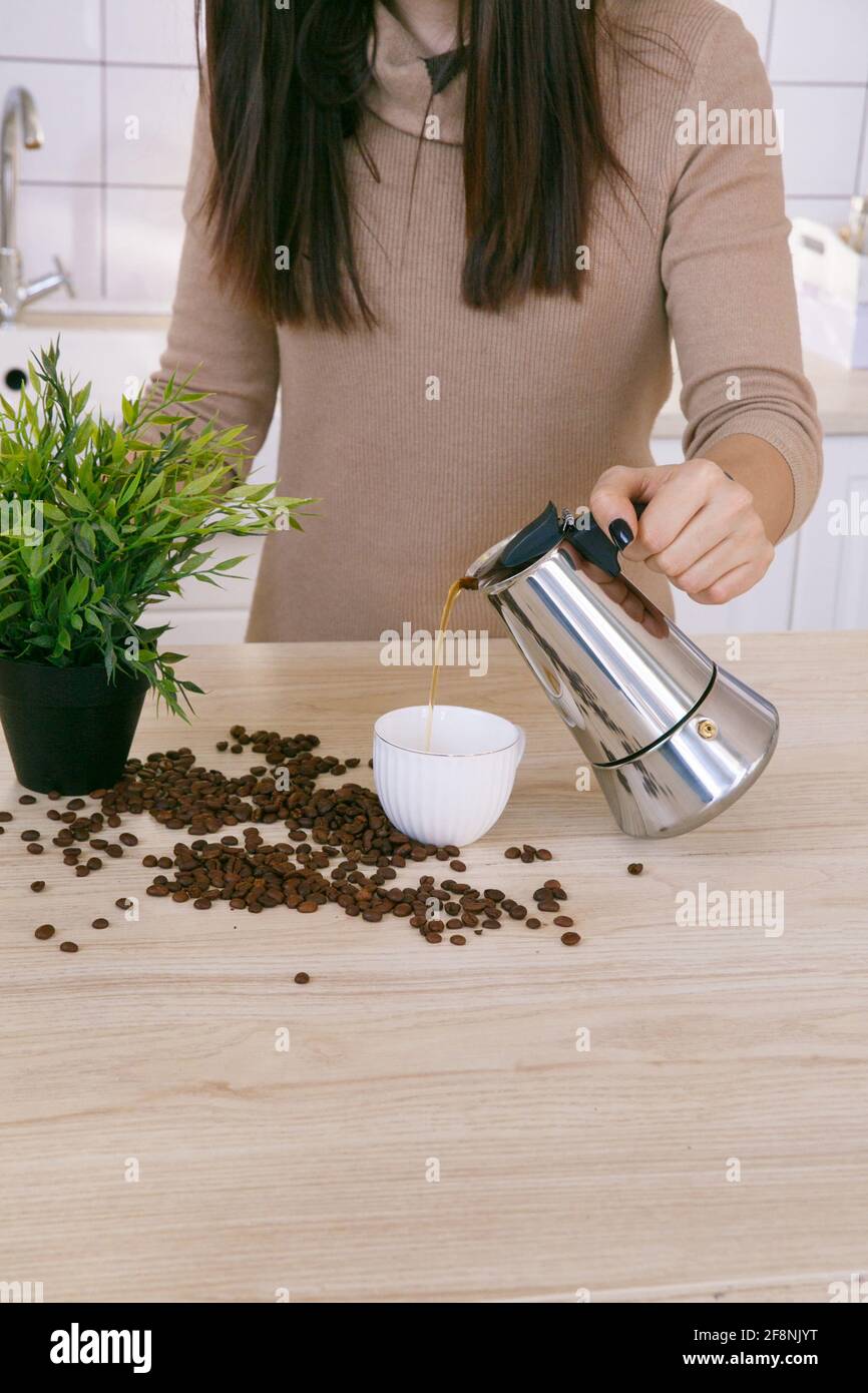 Woman in a light scandinavian kitchen pours coffee from a coffee machine into a mug in the morning Stock Photo