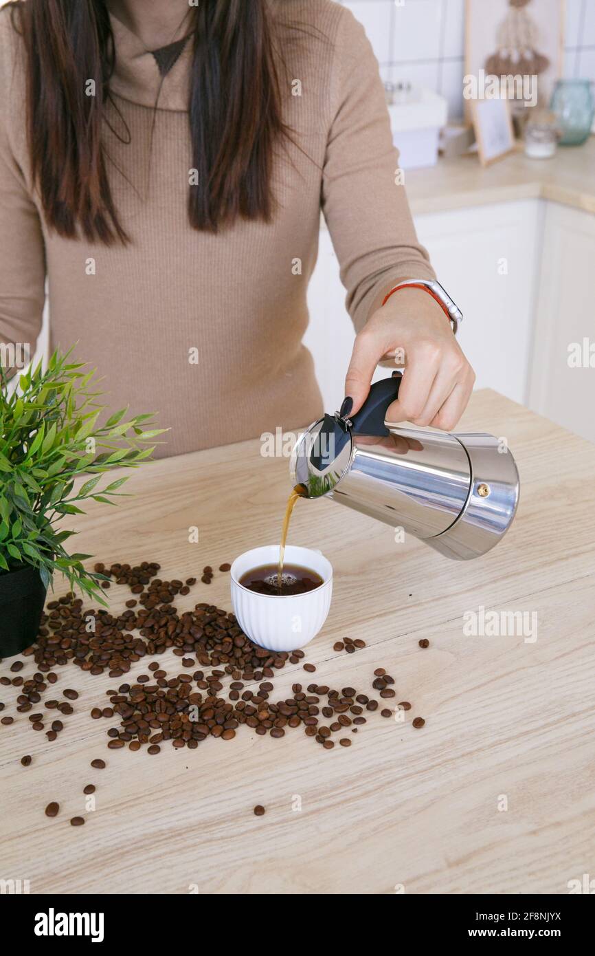 Woman in a light scandinavian kitchen pours coffee from a coffee machine into a mug in the morning Stock Photo