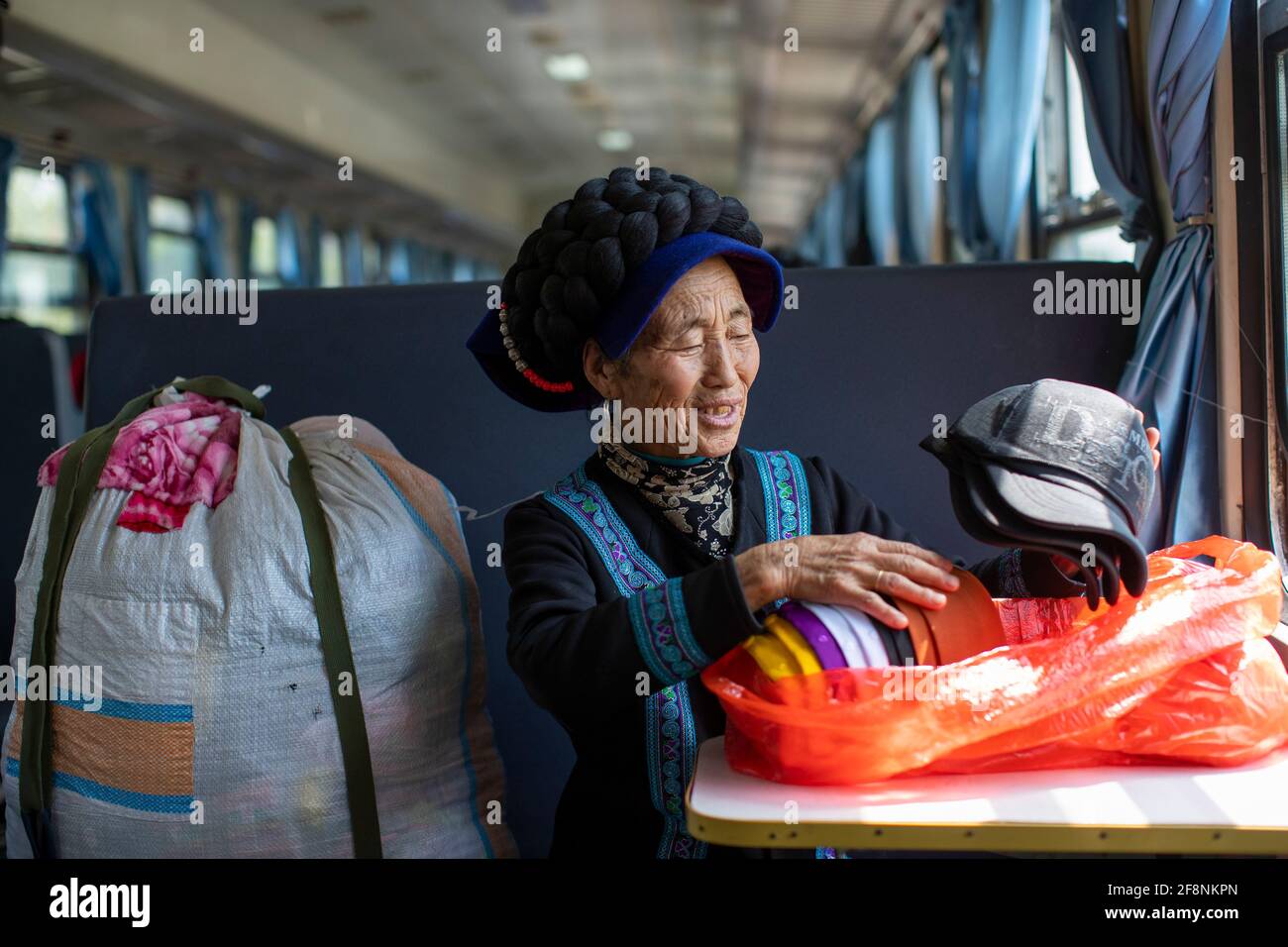 (210415) -- XICHANG, April 15, 2021 (Xinhua) -- A woman of Yi ethnic group arranges her goods purchased from Xichang City on the 5634 train in southwest China's Sichuan Province, April 12, 2021. As modern high-speed trains shoot past new stations throughout China, a pair of slow-speed trains still run through Daliang Mountains. The 5633/5634 trains run between Puxiong and Panzhihua of Sichuan Province with an average speed less than 40 km per hour. The journey with 26 stations in between takes eleven hours and four minutes, with the ticket prices ranging from 2 yuan to 25.5 yuan(about 0.3-3. Stock Photo