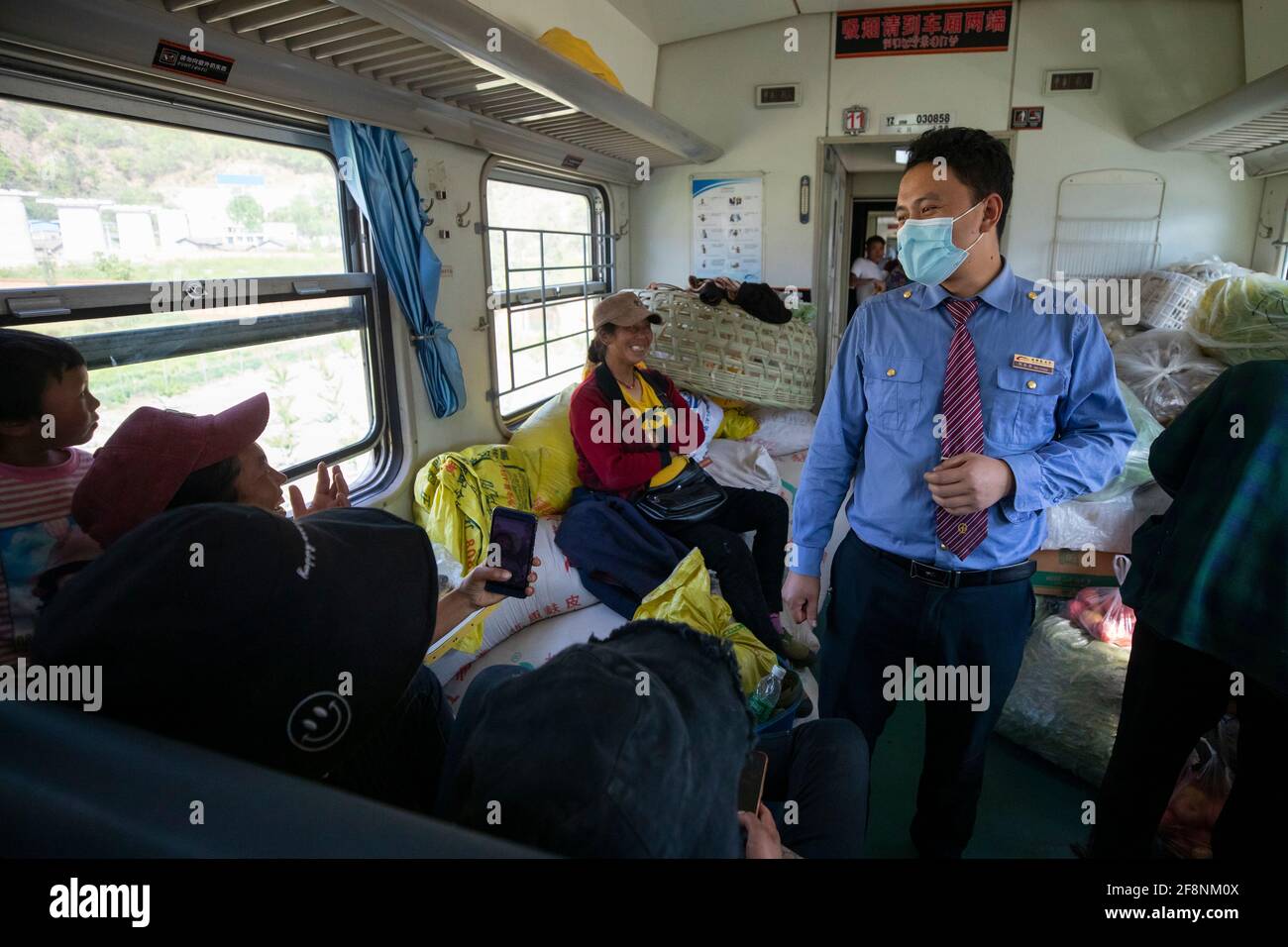 (210415) -- XICHANG, April 15, 2021 (Xinhua) -- A train steward of Yi ethnic group talks to passengers on the 5634 train in southwest China's Sichuan Province, April 12, 2021. As modern high-speed trains shoot past new stations throughout China, a pair of slow-speed trains still run through Daliang Mountains. The 5633/5634 trains run between Puxiong and Panzhihua of Sichuan Province with an average speed less than 40 km per hour. The journey with 26 stations in between takes eleven hours and four minutes, with the ticket prices ranging from 2 yuan to 25.5 yuan(about 0.3-3.9 U.S. dollars). Stock Photo