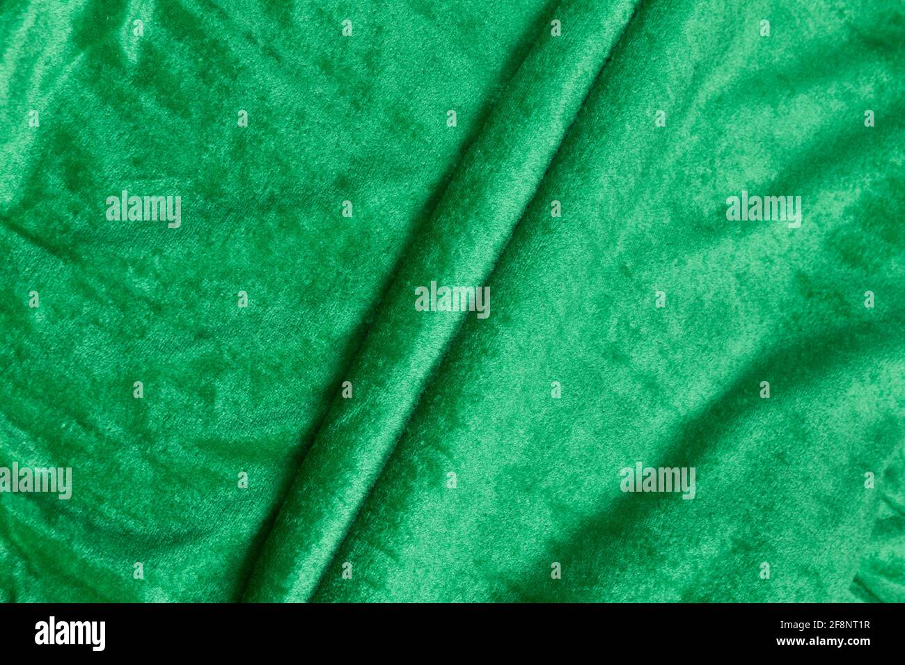 Colored green textile satin fabric folded in folds and waves with highlights and texture shimmers in the light Stock Photo