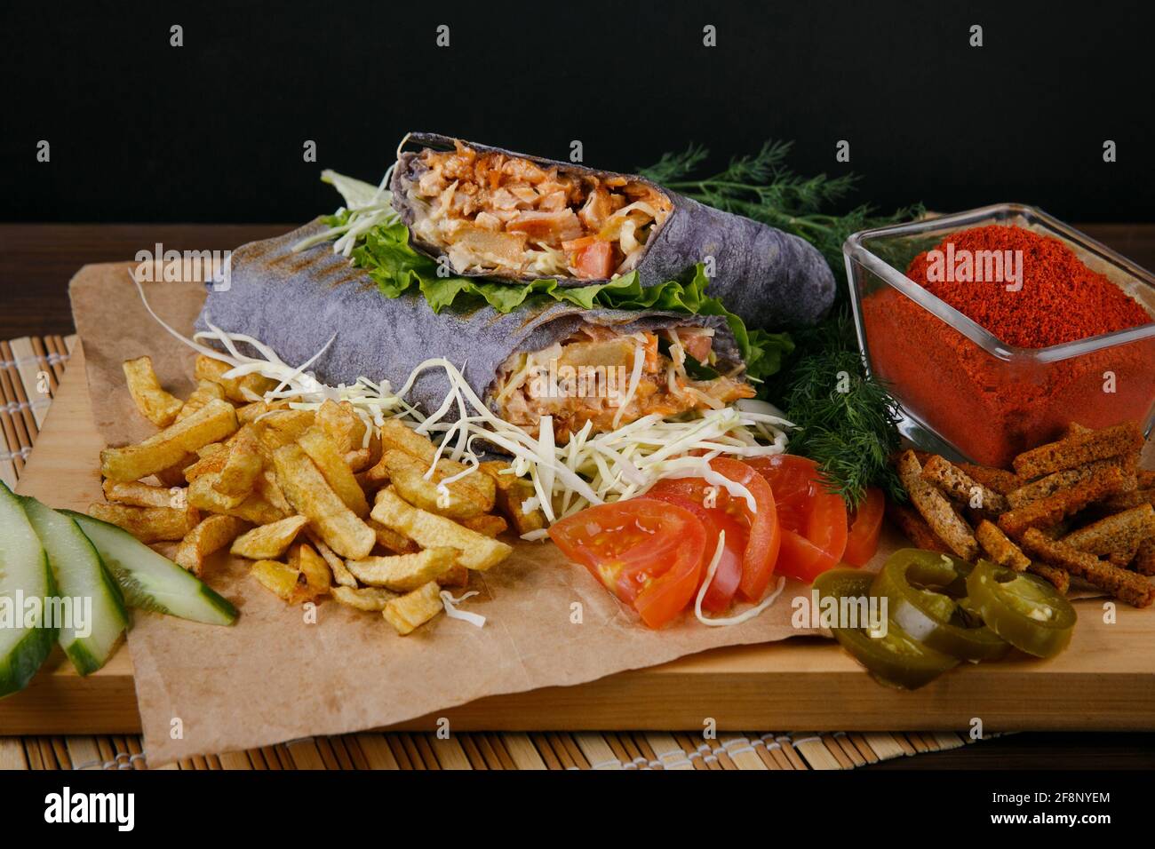 Fresh hot fragrant shawarma cut lies on a wooden board with vegetables, green leaves and fries on a black background Stock Photo