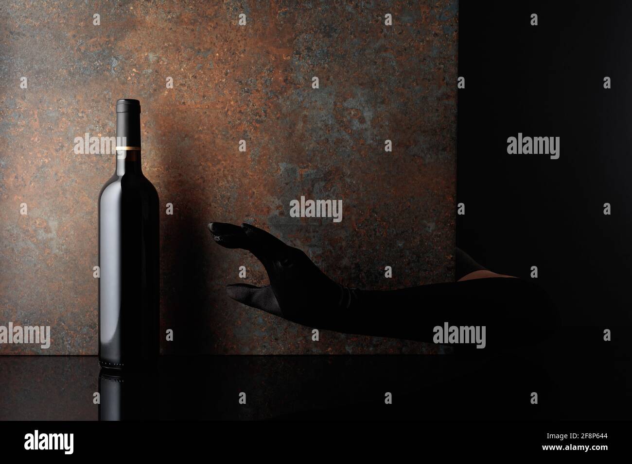 Woman hand in glove reaches for a bottle of red wine. A concept image on the theme of expensive wines. Copy space. Stock Photo