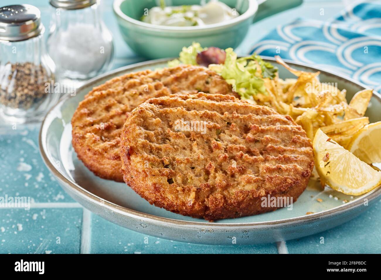Closeup of appetizing homemade fried fish patties and fries served with fresh lettuce and lemon on table with sauce Stock Photo