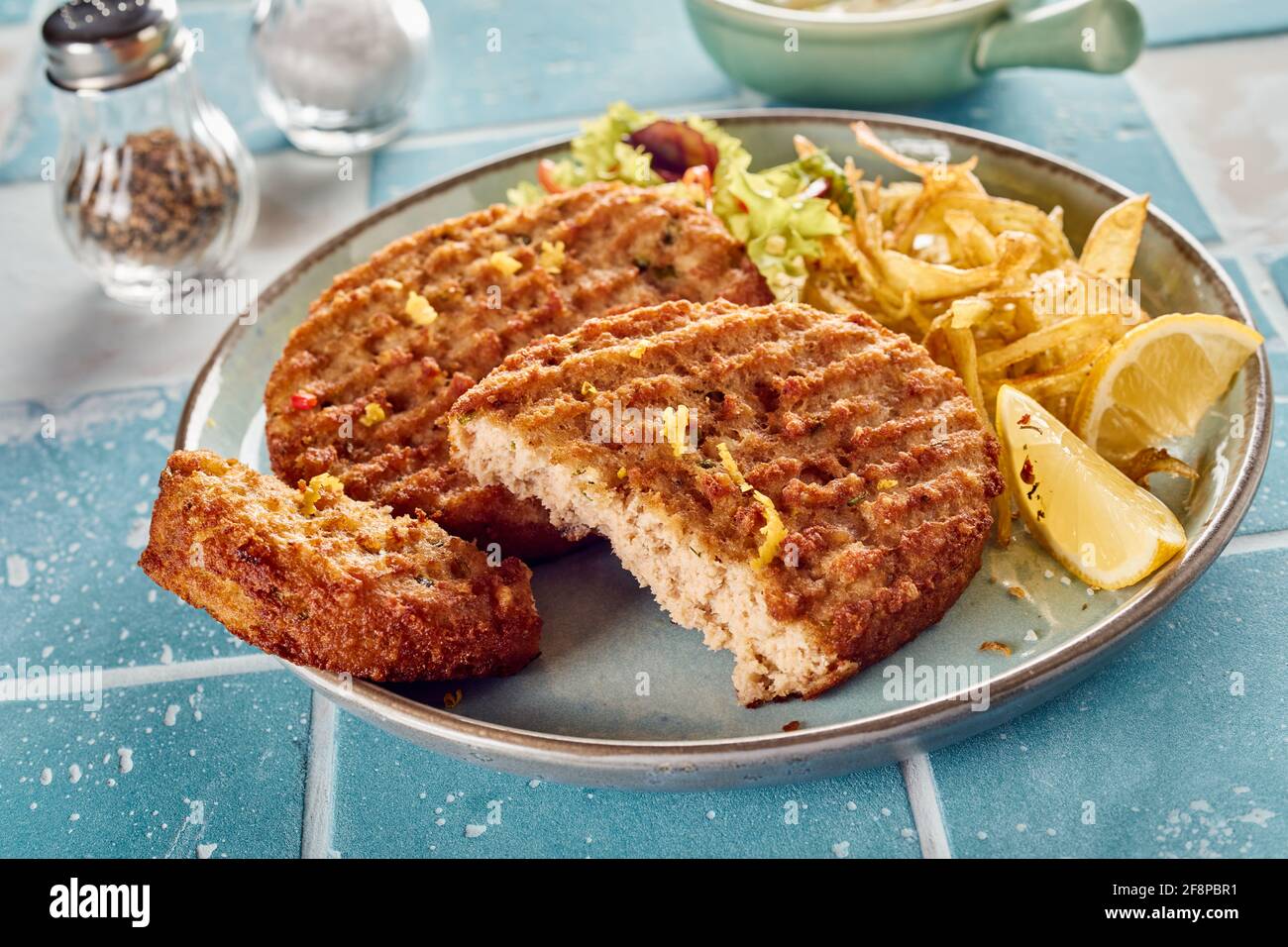 Closeup of appetizing homemade grilled fish patties with cut piece served on plate with fries and fresh lemon and lettuce Stock Photo
