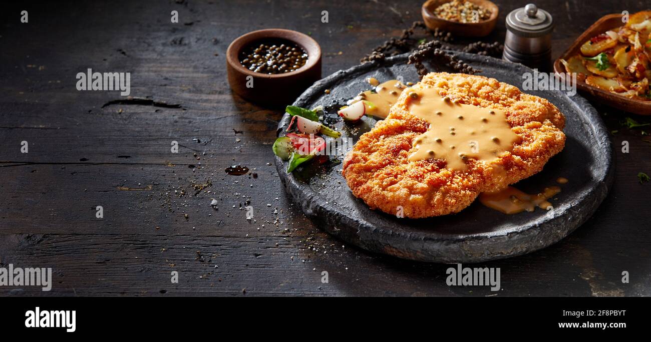 High angle of yummy fried breaded veal escalope with golden crust garnished with creamy spicy yellow sauce and fresh vegetables on wooden table Stock Photo