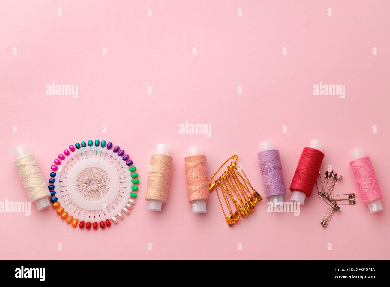 Sewing accessories including thread spools and pins on pink background ...