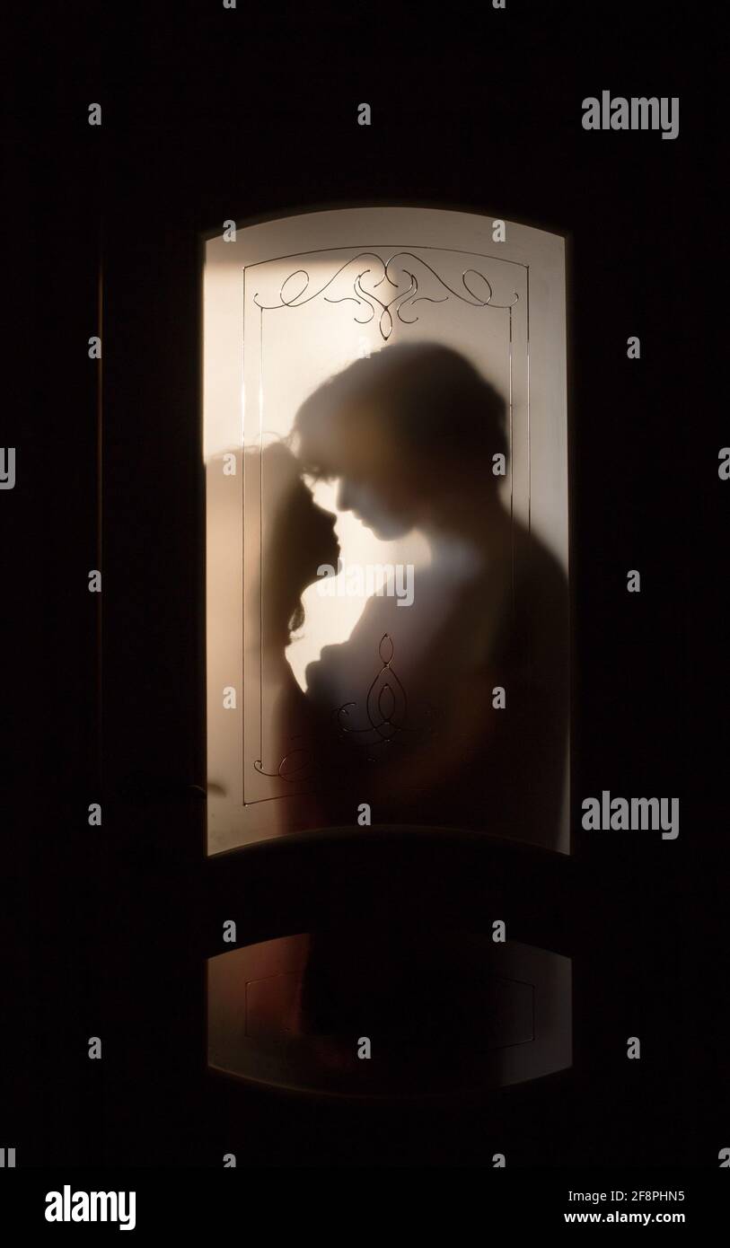 Silhouette of a loving young couple hugging while standing outside the door in the room. Shadows of a guy and a girl in the doorway. Relationships, fa Stock Photo