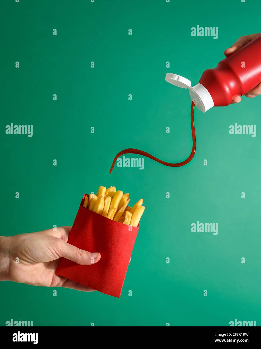Fries potatoes in red package in hand on green background with tomato