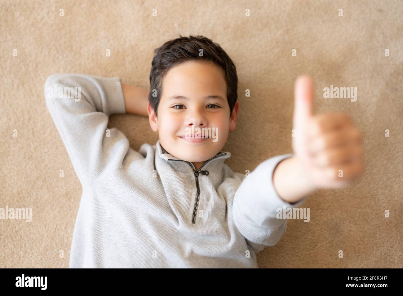 Top view of happy little boy lying on the floor with thumb up Stock