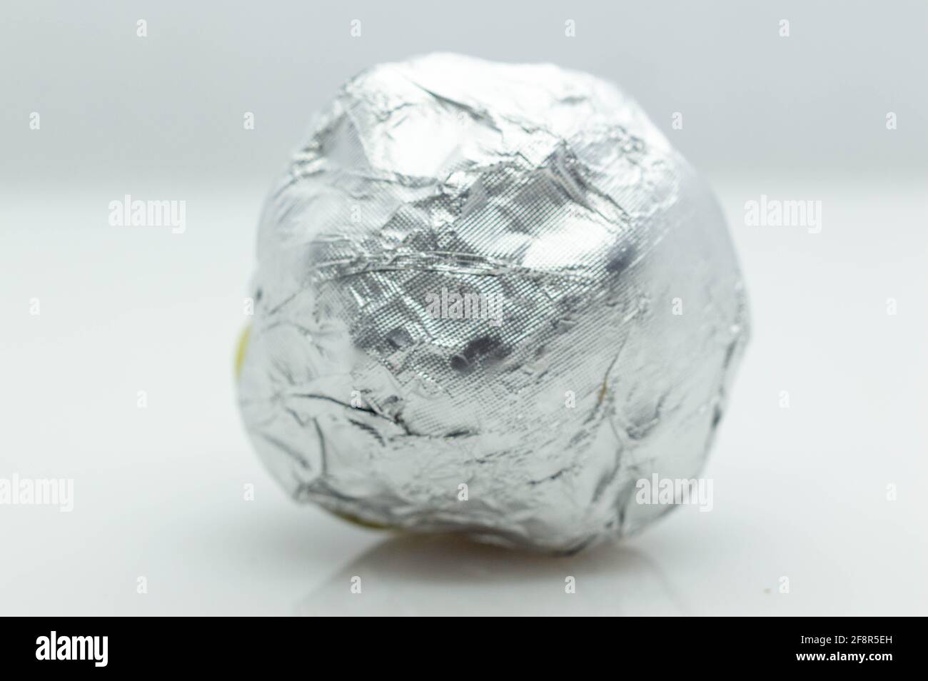 round chocolate candy in a white shiny package on a gray background . isolated, close-up Stock Photo