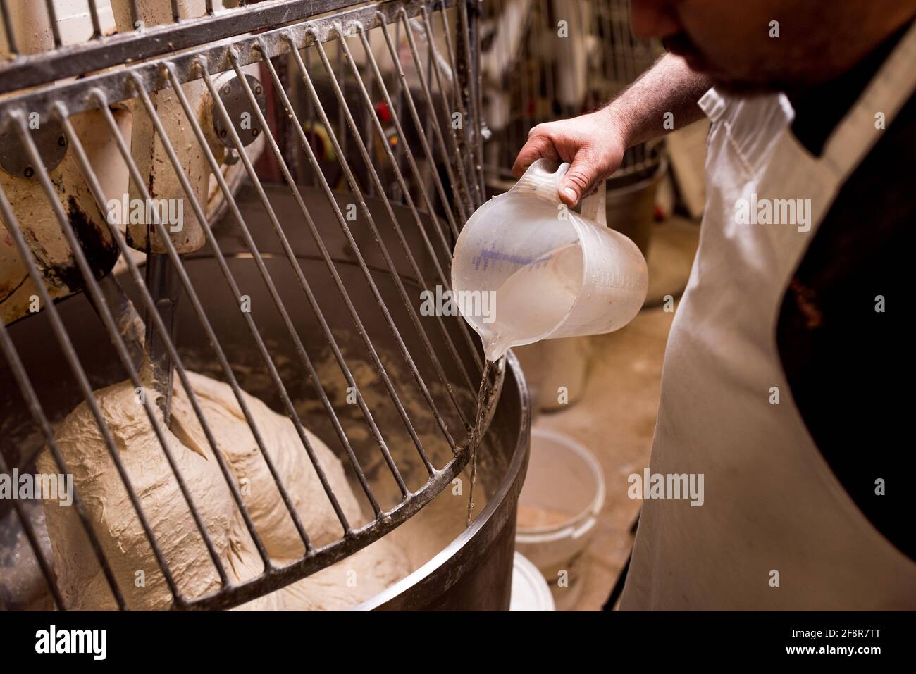 close up baker putting water inside bread dough preparation inside