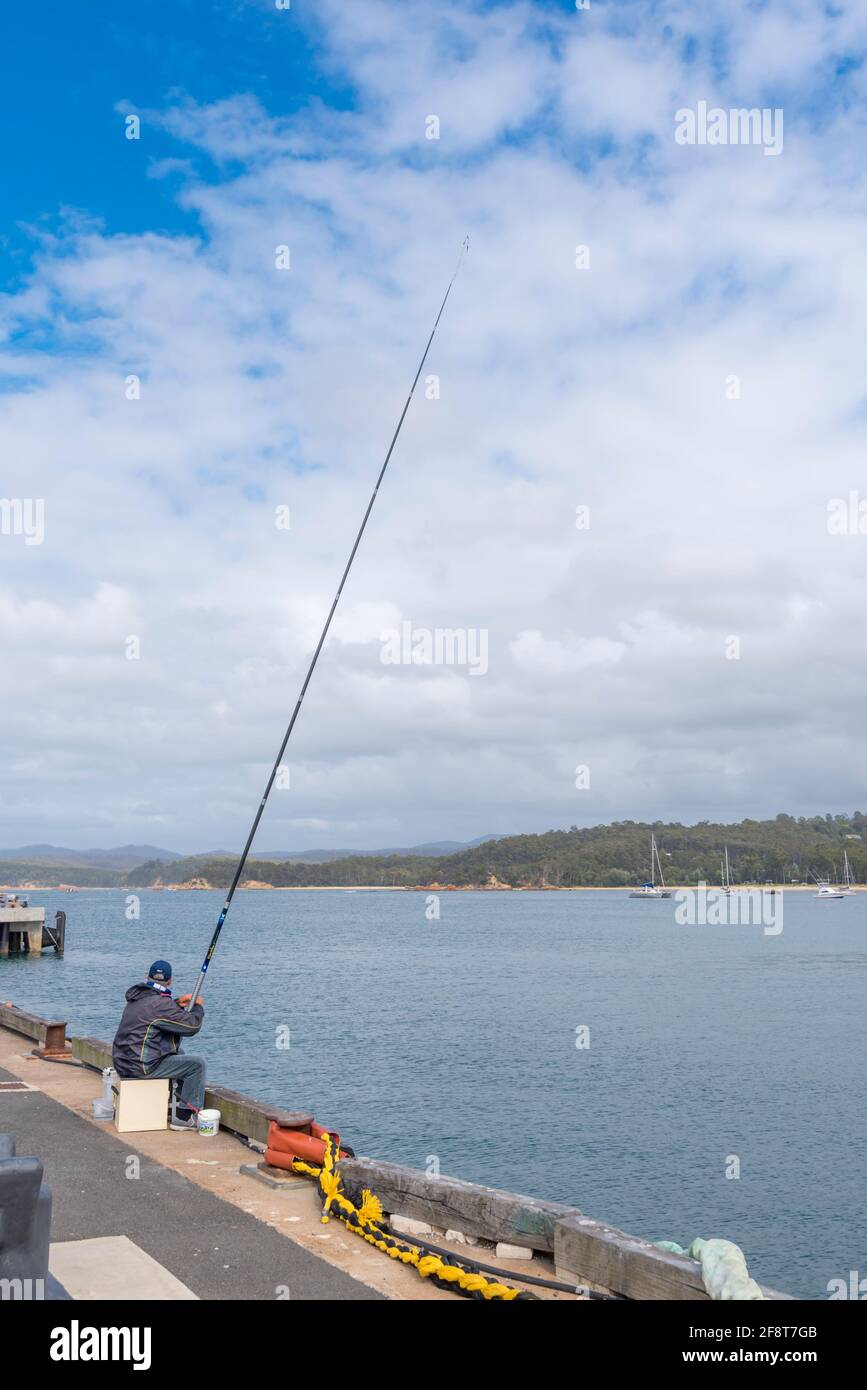 A man fishing from the wharf with a very large fishing rod at the Port of Eden on the New South Wales south coast of Australia Stock Photo