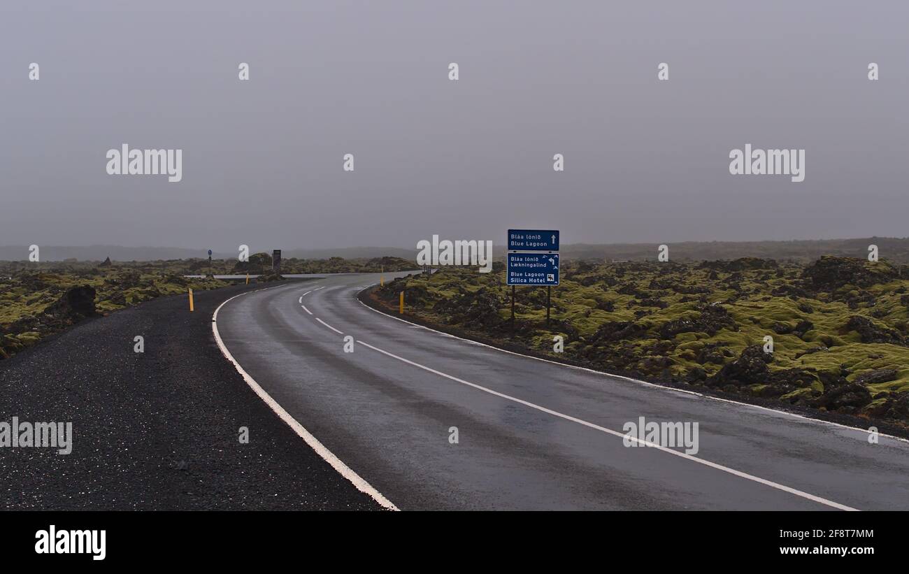 Empty country road between lava field with road sign showing the way to the Blue Lagoon and Silica Hotel in winter season on foggy day. Stock Photo